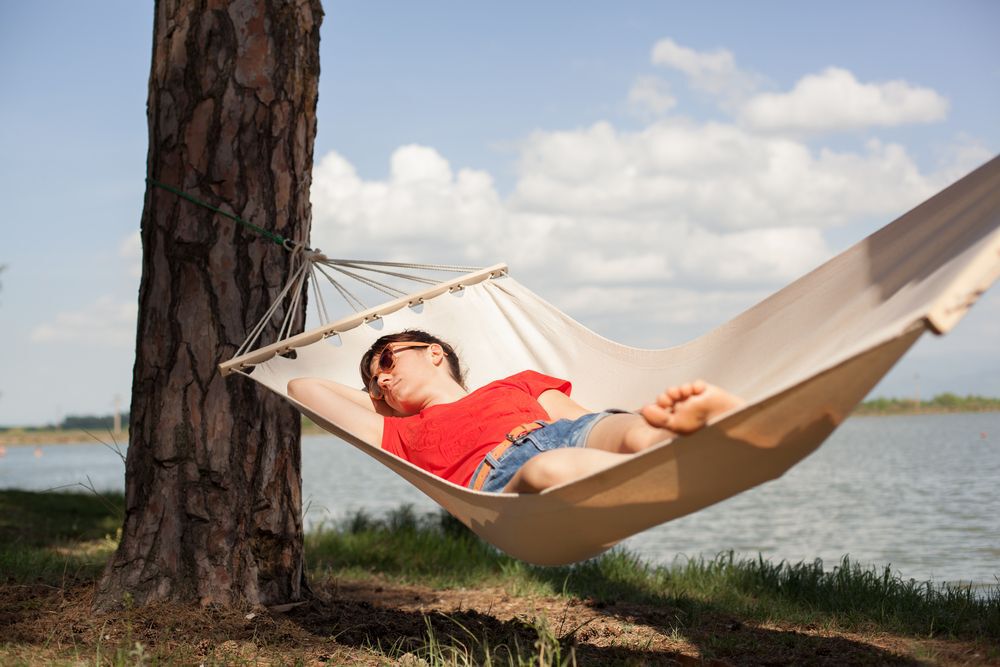 Person in a red shirt laying in a hammock by a lake.