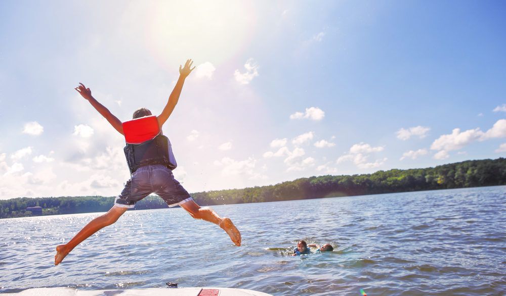 Kid in a red life jacket jumping into a lake.