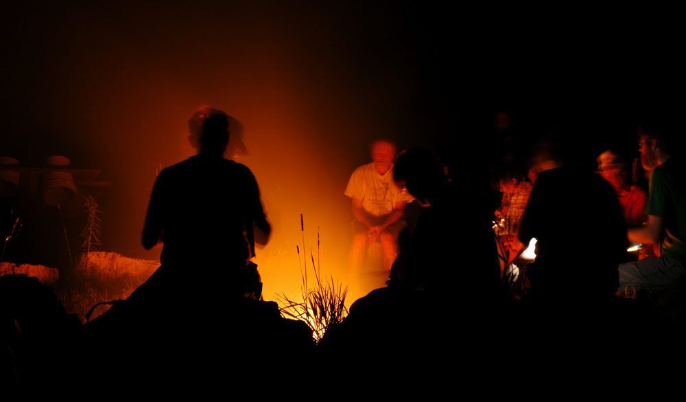 Silhouettes of people sitting around a campfire.