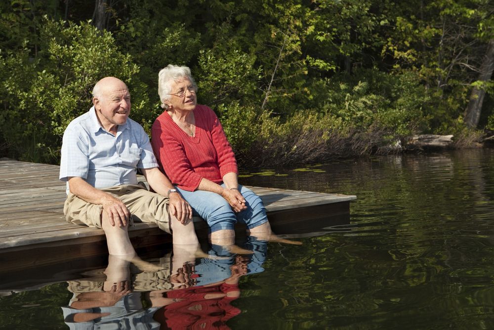 Older couple sitting on a wooden dock with their feet in the water.