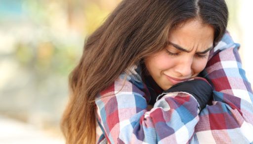 Upset teen girl in a plaid shirt with her arms crossed over her knees.