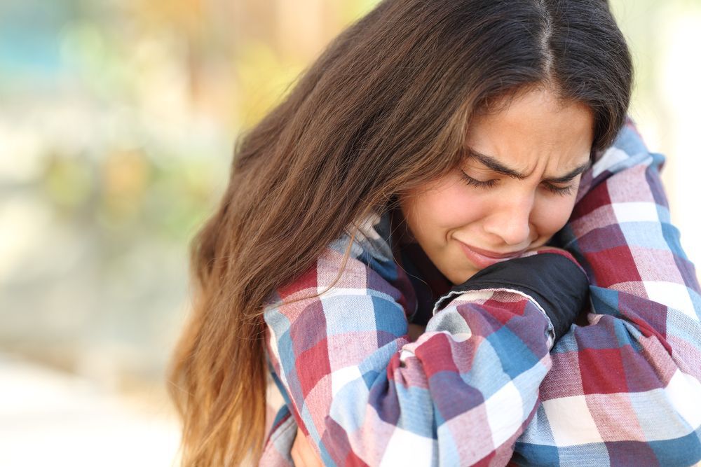 Upset teen girl in a plaid shirt with her arms crossed over her knees.