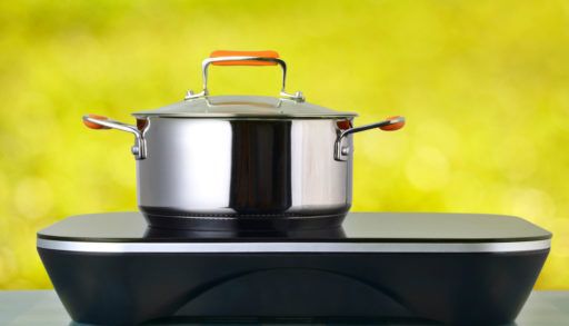 Induction cooktop with a pot on top of it on a blue gingham table against a yellow background.