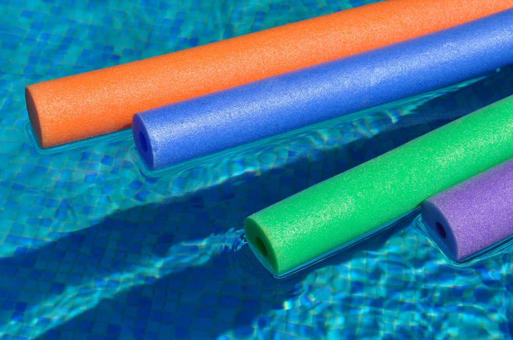 Coloured pool noodles floating in a pool.