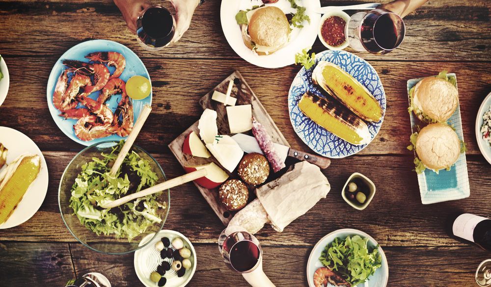 Bird's-eye-view of a wooden table filled with food with the occasional hand reaching for something.