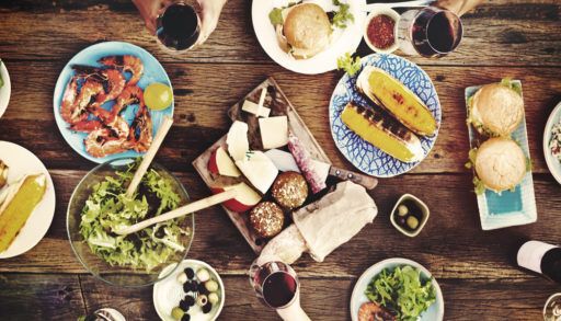 Bird's-eye-view of a wooden table filled with food with the occasional hand reaching for something.