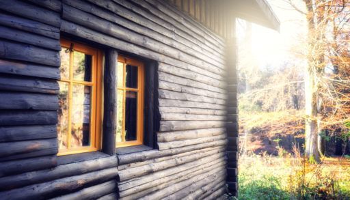 Dark wooden cabin with sun peaking around the corner.