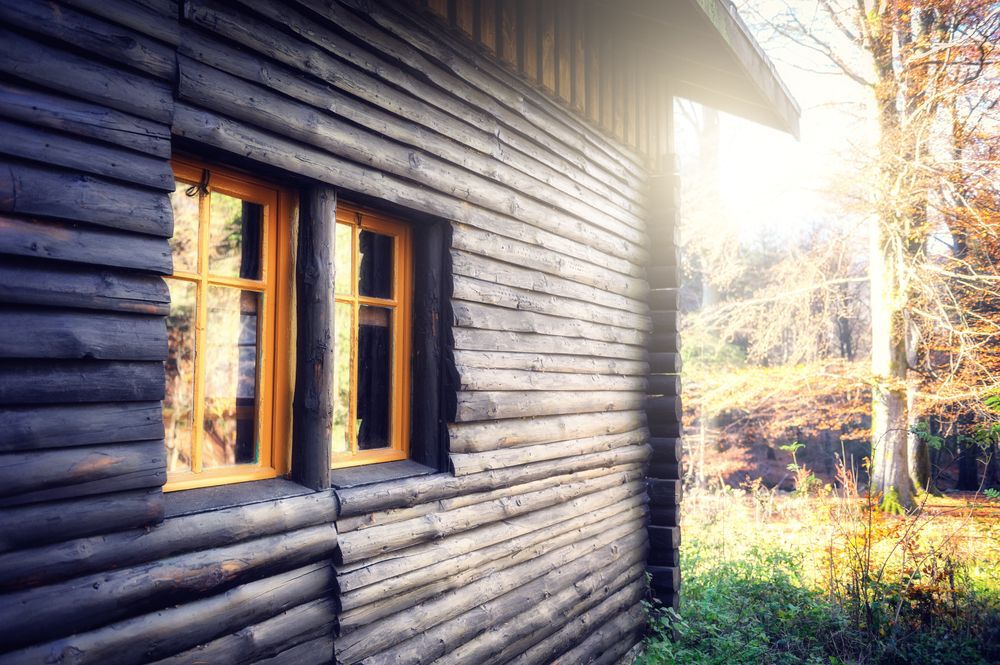 Dark wooden cabin with sun peaking around the corner.