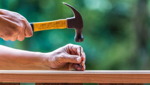 Person poised to hammer a nail into wood.