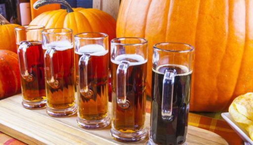 Beer flight on a wooden board in front of orange pumpkins.