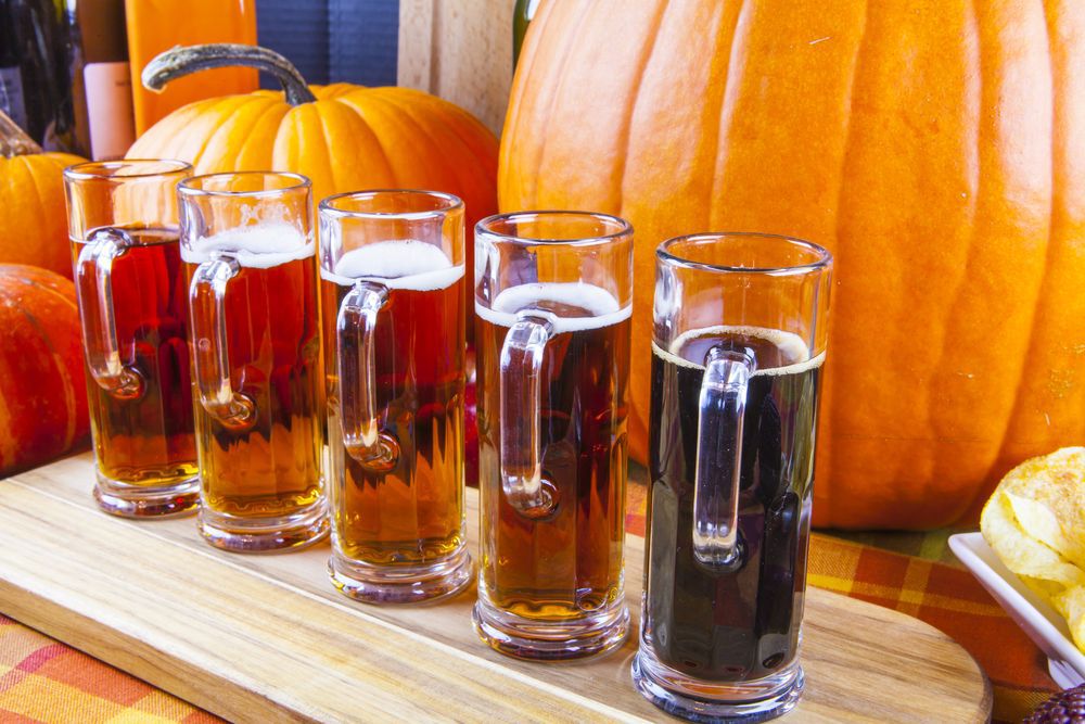 Beer flight on a wooden board in front of orange pumpkins.