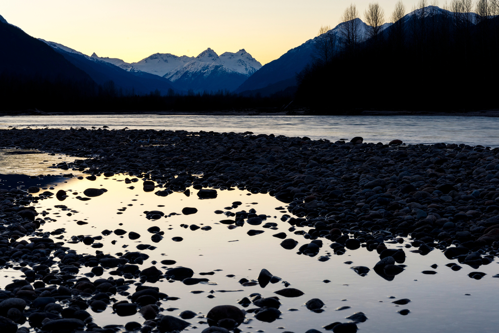 Mount Meager at sunset surrounded by silhouetted trees and a lake.