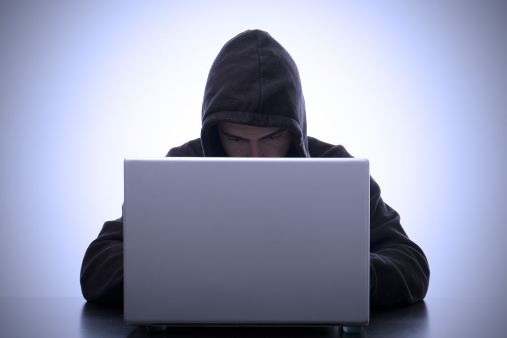 Hacker in a grey hoodie with the hood up on a computer.