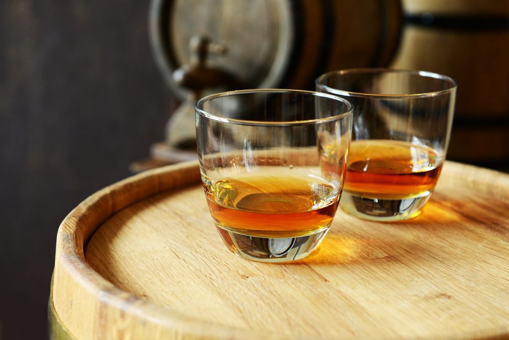 Two glasses of brandy sitting on a wooden barrel.
