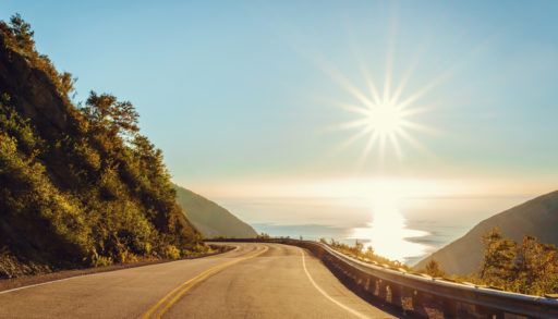 Road bordered by a hill and a cliff that overlooks the ocean in Cape Breton, Nova Scotia, Canada.