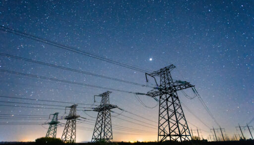 High voltage power line against a starry night sky.