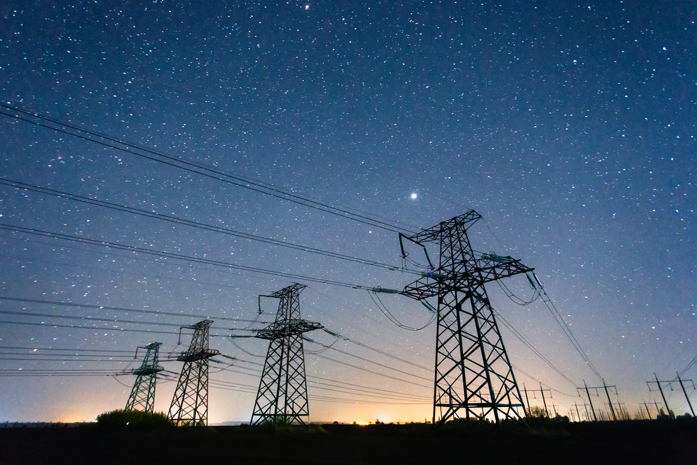 High voltage power line against a starry night sky.