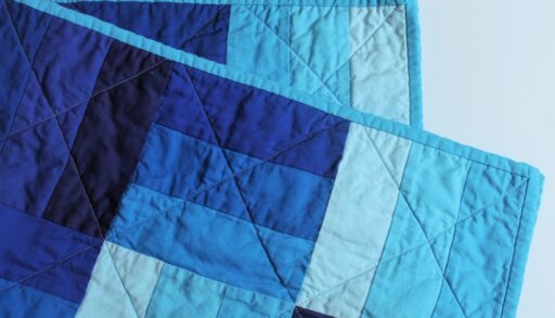 A folded quilt coloured varying shades of blue.