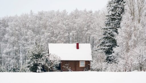 Wooden cabin with a red chimney covered in snow and buried in a winter forest.