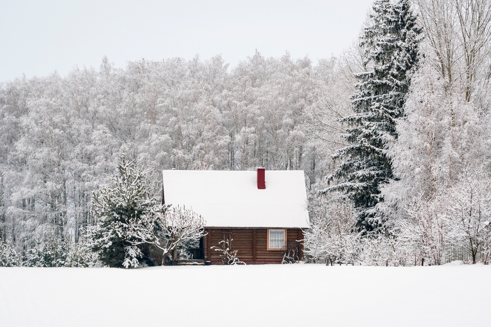 Wooden cabin with a red chimney covered in snow and buried in a winter forest.