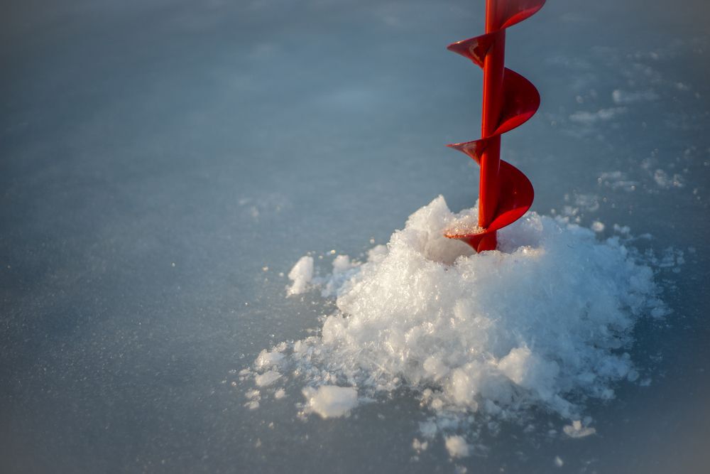 Red ice auger drilling through ice.
