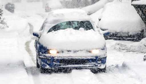 Blue car covered in snow improperly cleared off driving on the road.