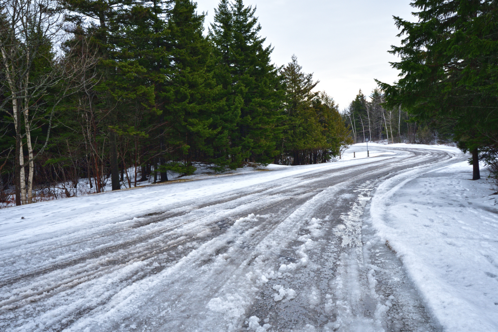 Slushy snow covered road bordered by trees.
