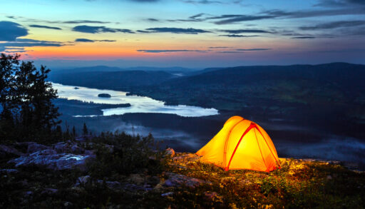 Tent lit up at dusk on top of a rocky mountain.