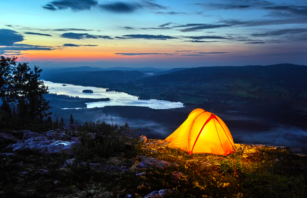Tent lit up at dusk on top of a rocky mountain.