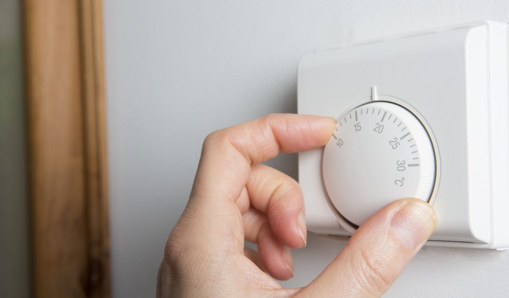 Person adjusting a white thermostat on the wall.