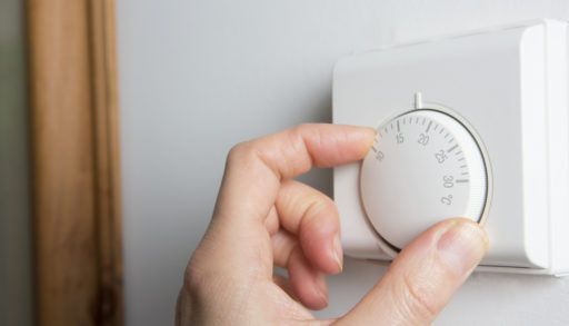 Person adjusting a white thermostat on the wall.