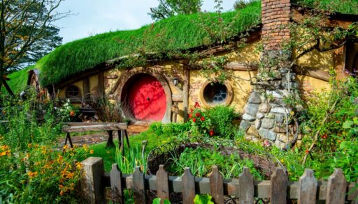 Hobbit hole with a red circular door and stone walls covered in moss and overgrowth.