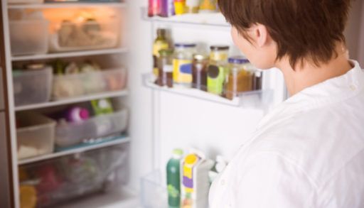 Woman in a white shirt looking inside her full fridge.