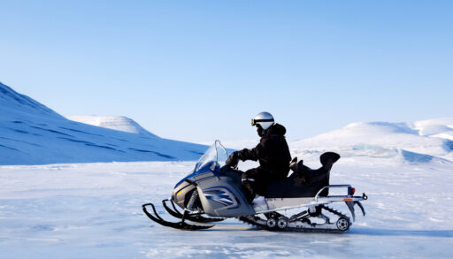 Person on a snowmobile riding across a winter mountain landscape.