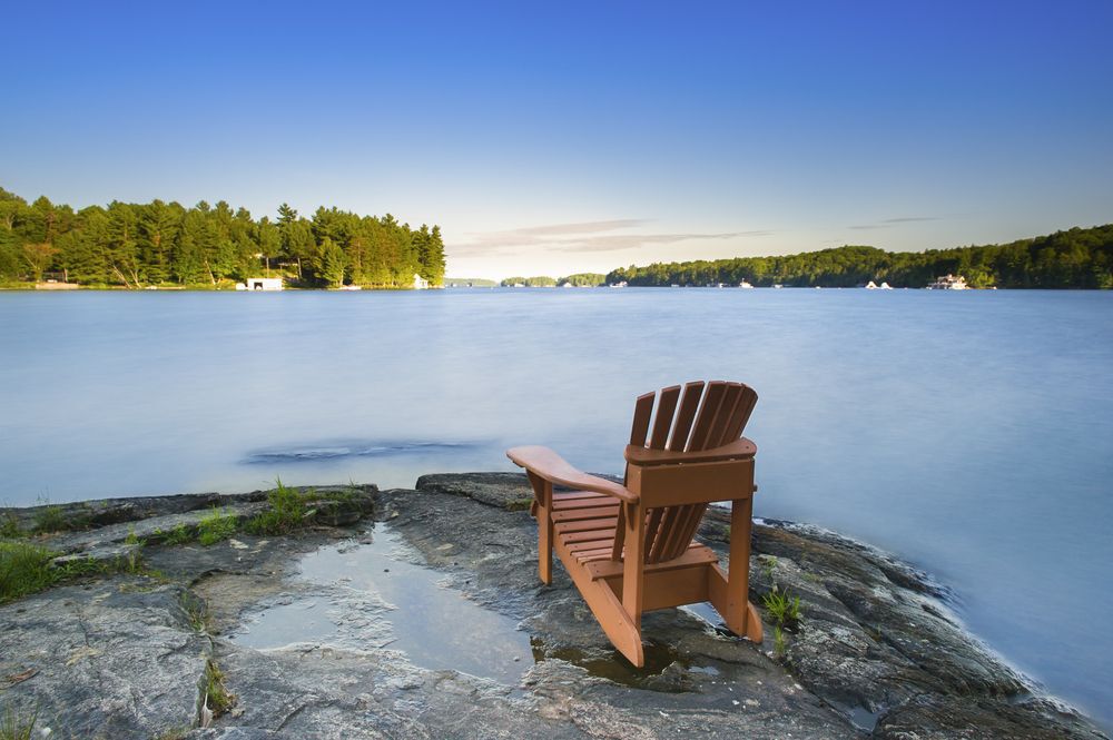 Adirondack chair on a rock by a lake in cottage country.