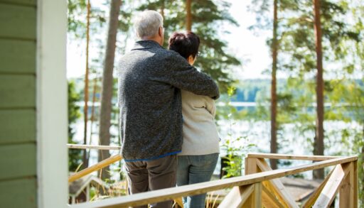 Old couple standing on the front porch of their cottage overlooking a lake.