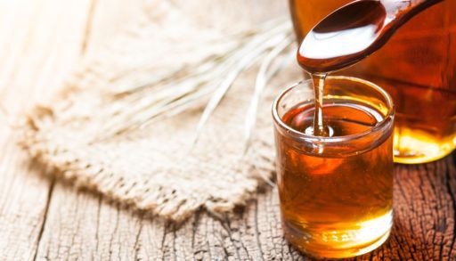Glass jar of maple syrup on a wooden table.