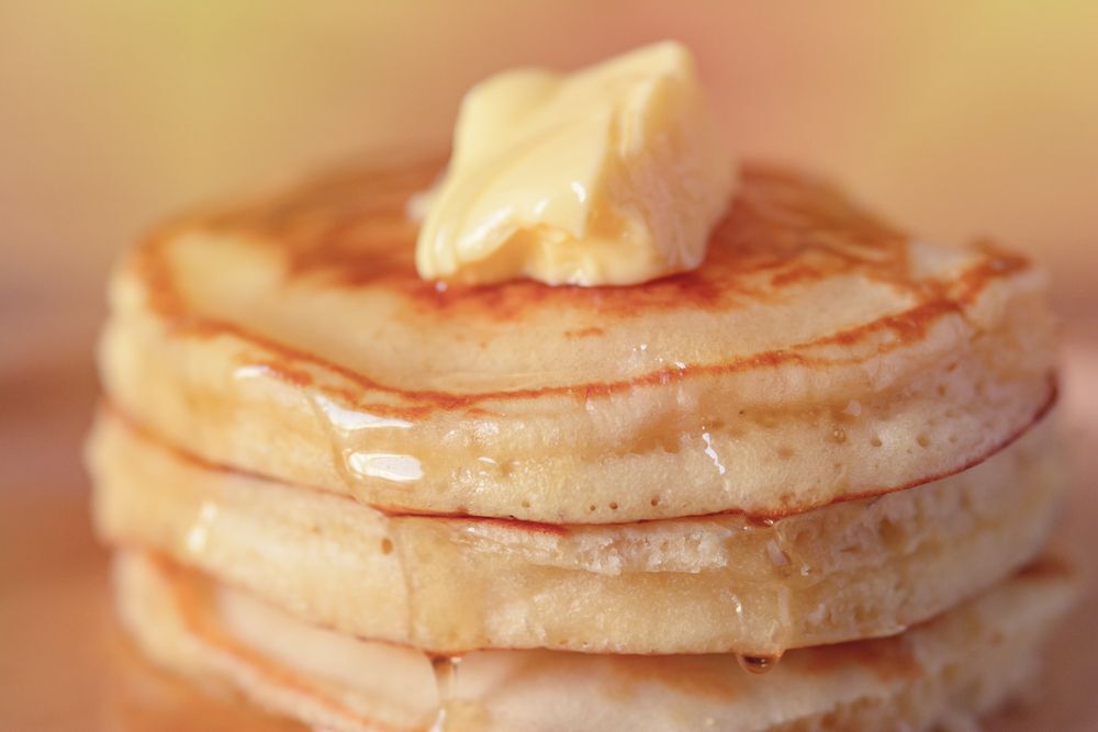 Close-up of a stack of pancakes with maple syrup and butter on top.