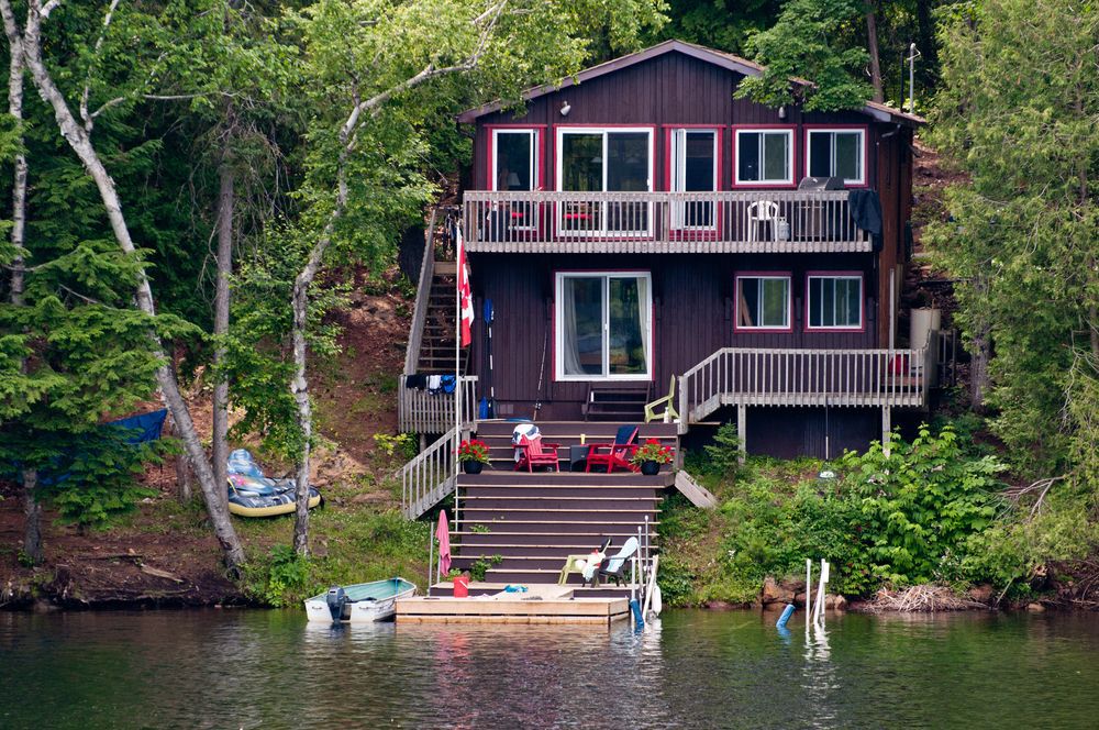 Lakeside brown cottage with red trim nestled in green foliage.