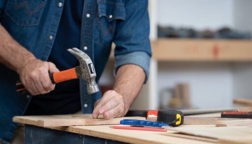 Man hammering a nail into a piece of wood in a workshop.