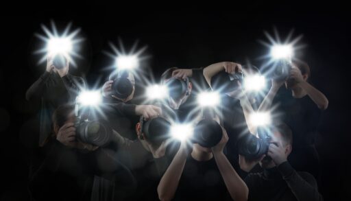Group of photographers with cameras flashing on a black background.