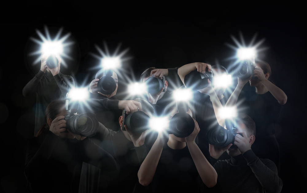 Group of photographers with cameras flashing on a black background.
