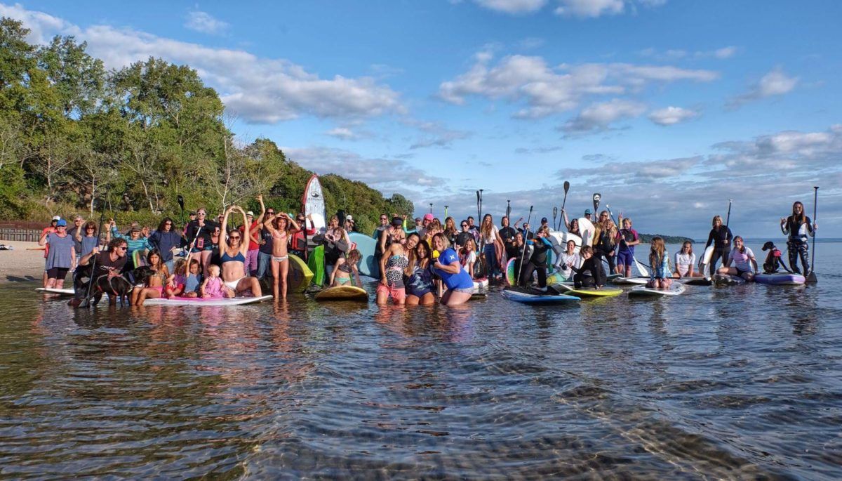 Large group of women posed for group photo with boards in the lake