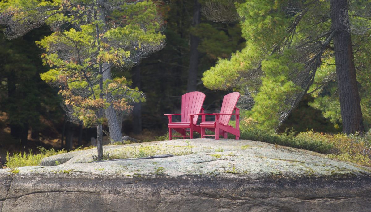 Two red Muskoka chairs on a rock
