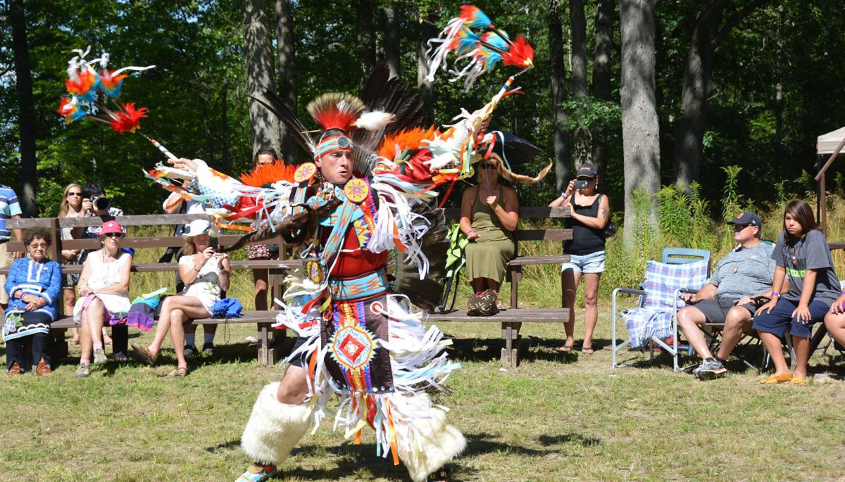 A man in pow wow regalia dances outside