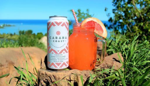 A can of Cabana Coast VOdka Greyhound and a mason jar cocktail sit in front of a lake