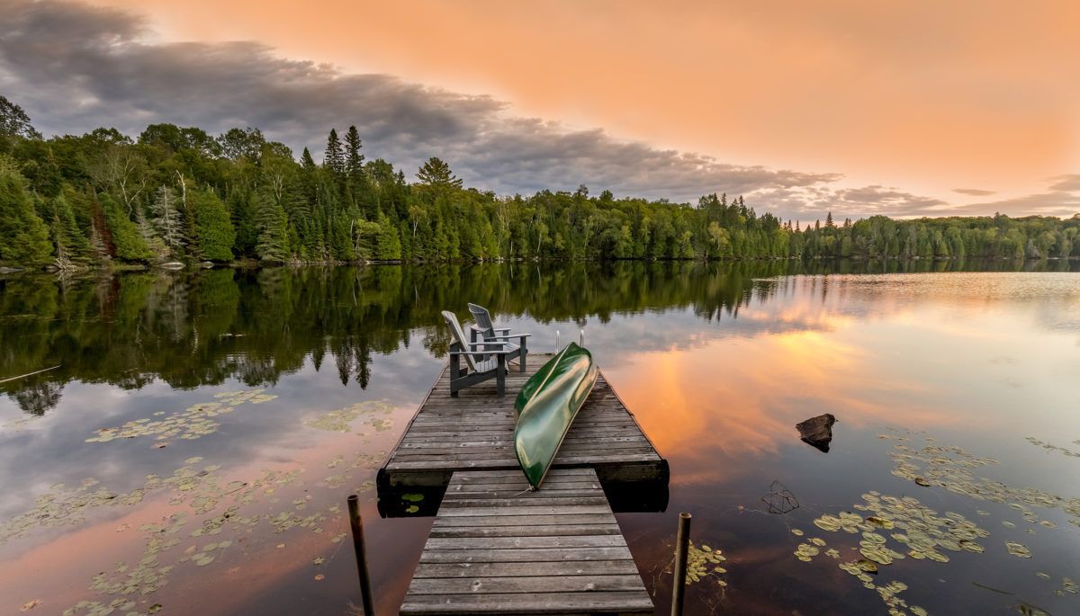 Looking down a dock with a green canoe on a lake at sunset.