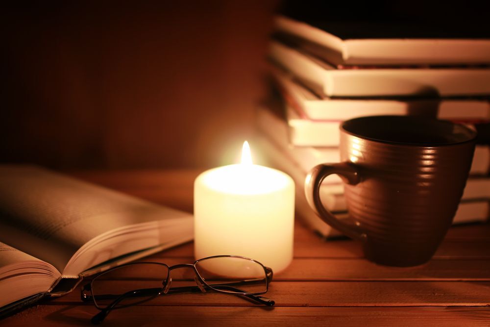 A pile of books and reading glasses illuminated by candelight