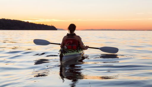 Girl paddling in a kayak on a lake at sunset.