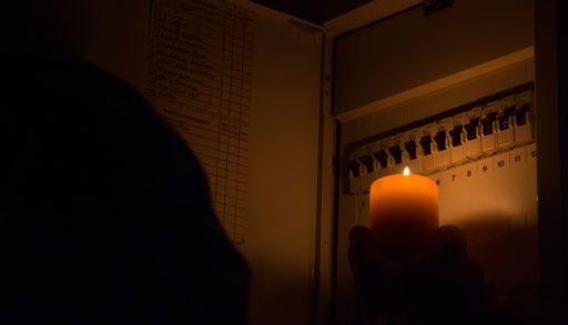 A person holds a candle up to check a breaker box in the dark